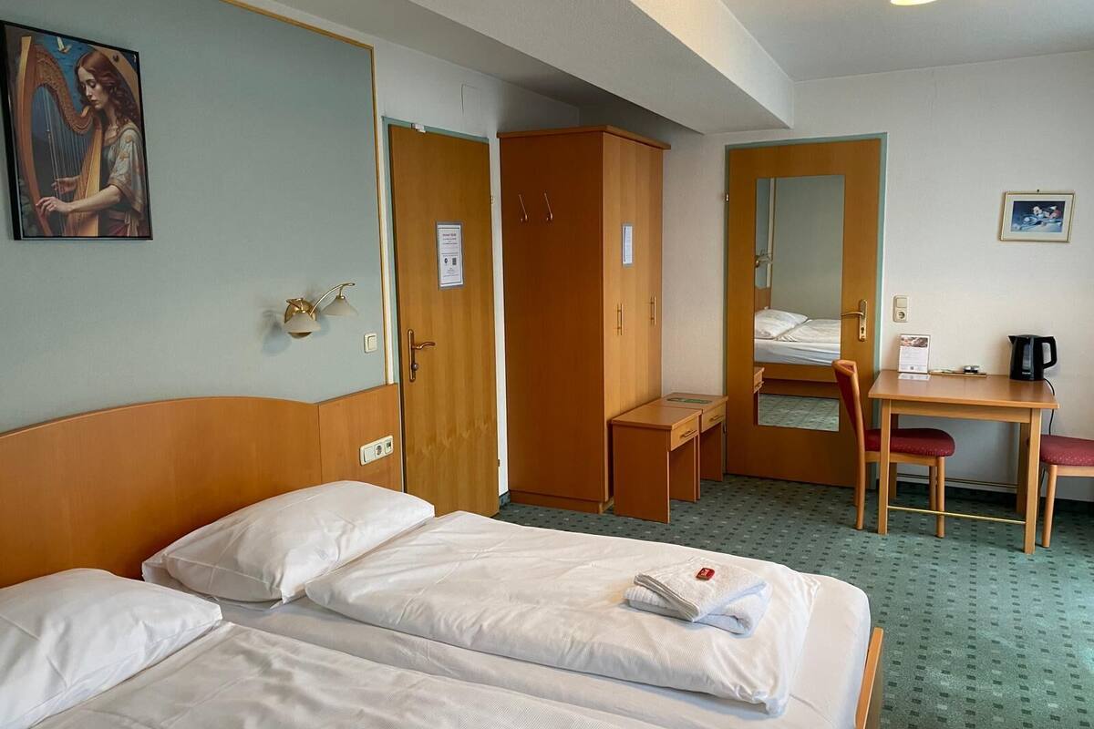 Ein Hotelzimmer mit zwei Betten, einem Schreibtisch, einem Stuhl, einem Kleiderschrank und einem Bild an der Wand.