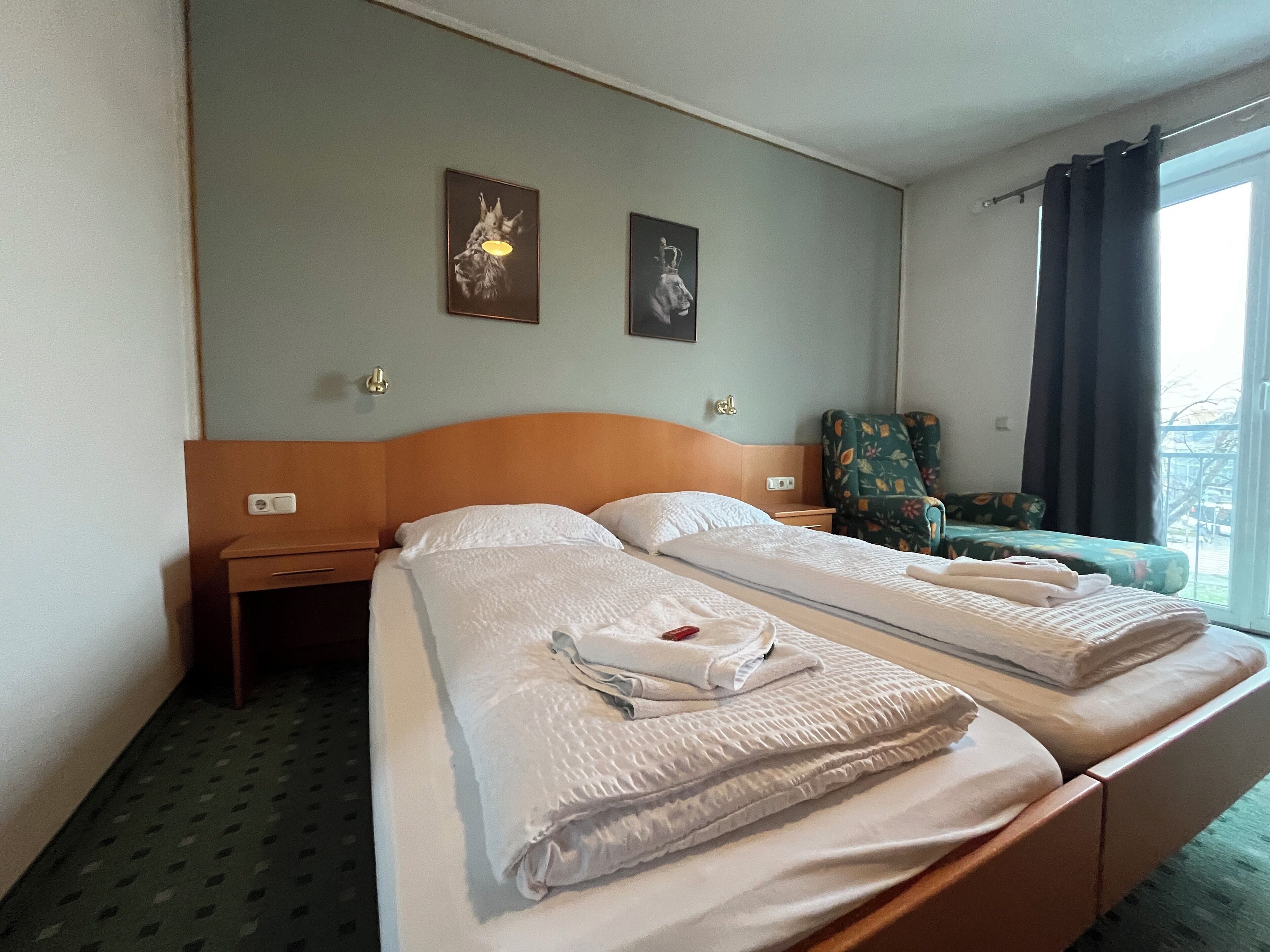Una habitación de hotel con dos camas, una mesita de noche, una silla y dos obras de arte en la pared.
