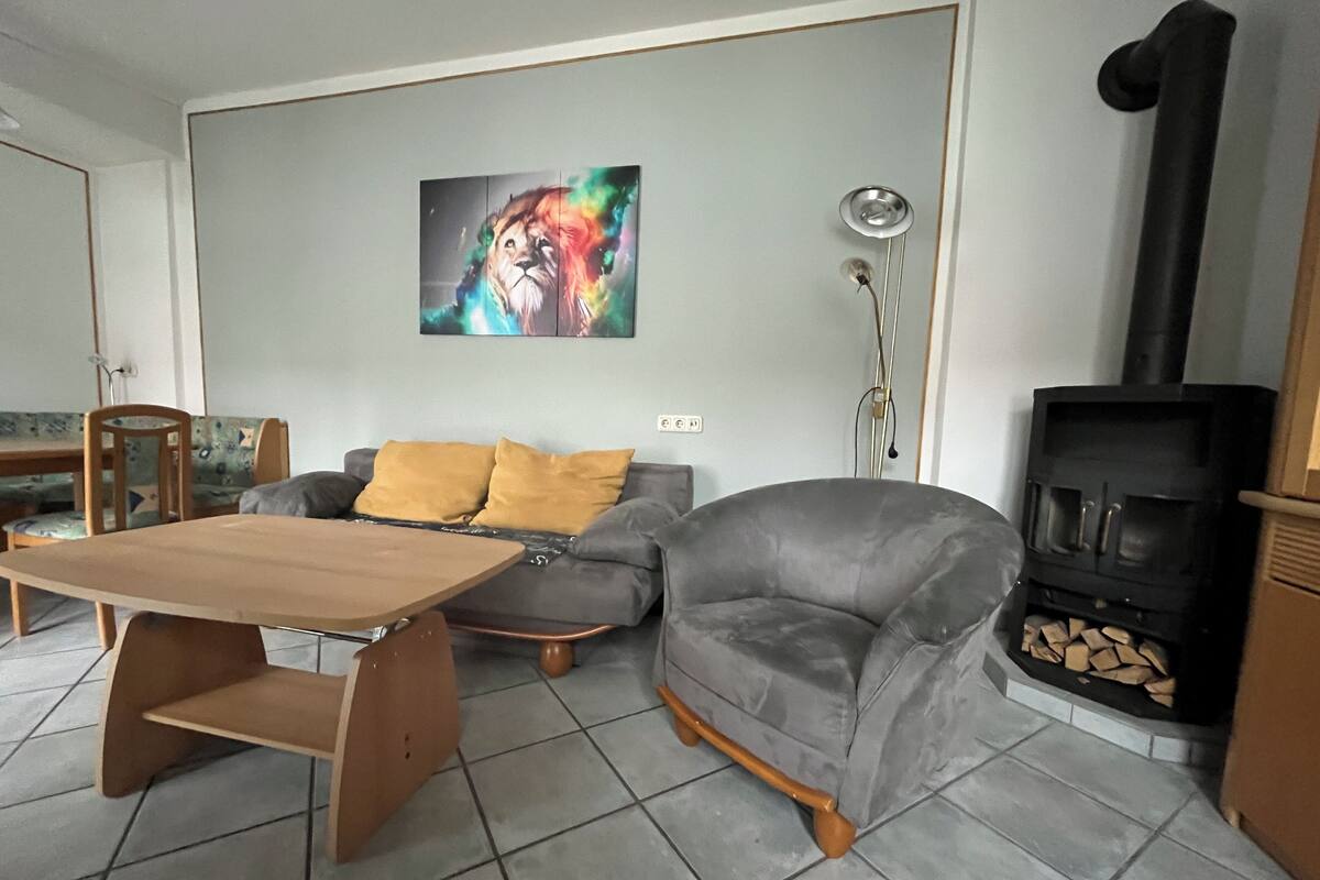 Ein Wohnzimmer mit grauem Sofa, einem Holztisch, einem Bild an der Wand und einem schwarzen Kaminofen.