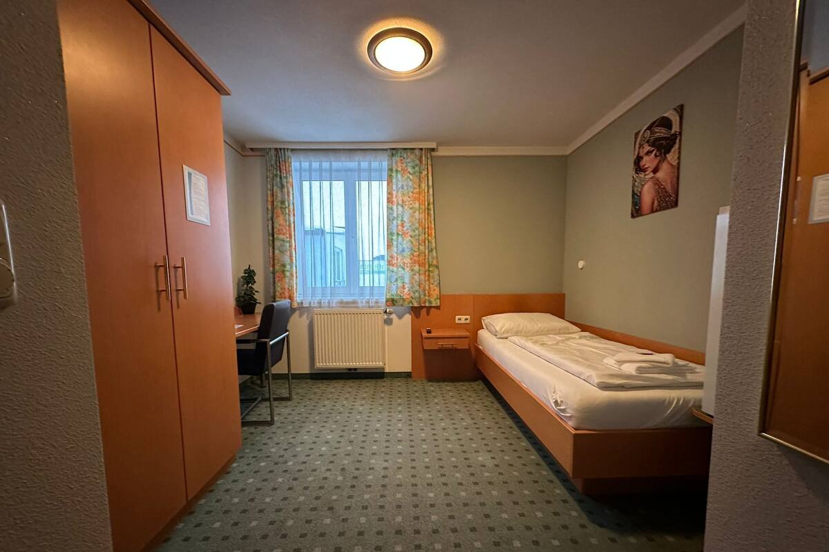 Ein kleines Hotelzimmer mit einem Einzelbett, einem Schreibtisch und einem Stuhl.