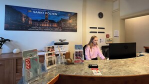 Un mostrador de recepción de hotel con un cartel de bienvenida grande, un folleto con un plano de la ciudad y un terminal de pago digital.