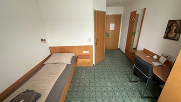 Habitación de hotel con una cama individual, un escritorio, una silla, un espejo y una puerta que da a otra habitación.