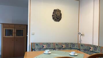 Un comedor con una mesa de madera, dos sillas, un banco con cojín estampado y una cabeza de león decorativa en la pared.