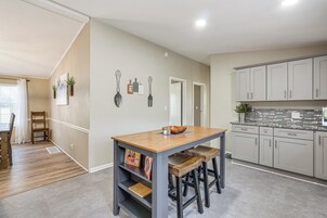 Una cocina moderna con una mesa de madera y taburetes de bar, armarios de colores claros y decoración en la pared.