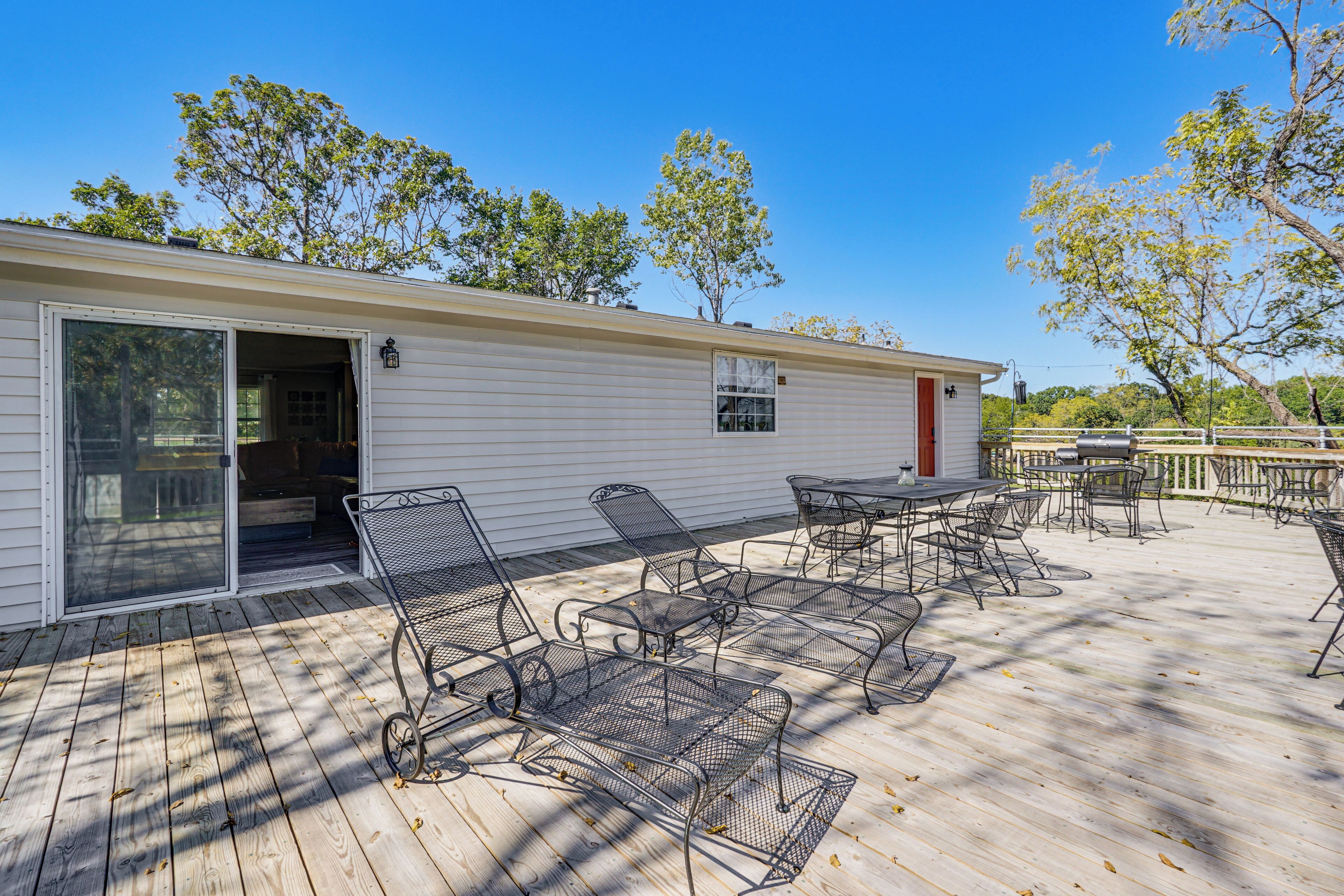 A covered outdoor patio with metal chairs and tables, a sliding glass door entrance, and a white building in the background.