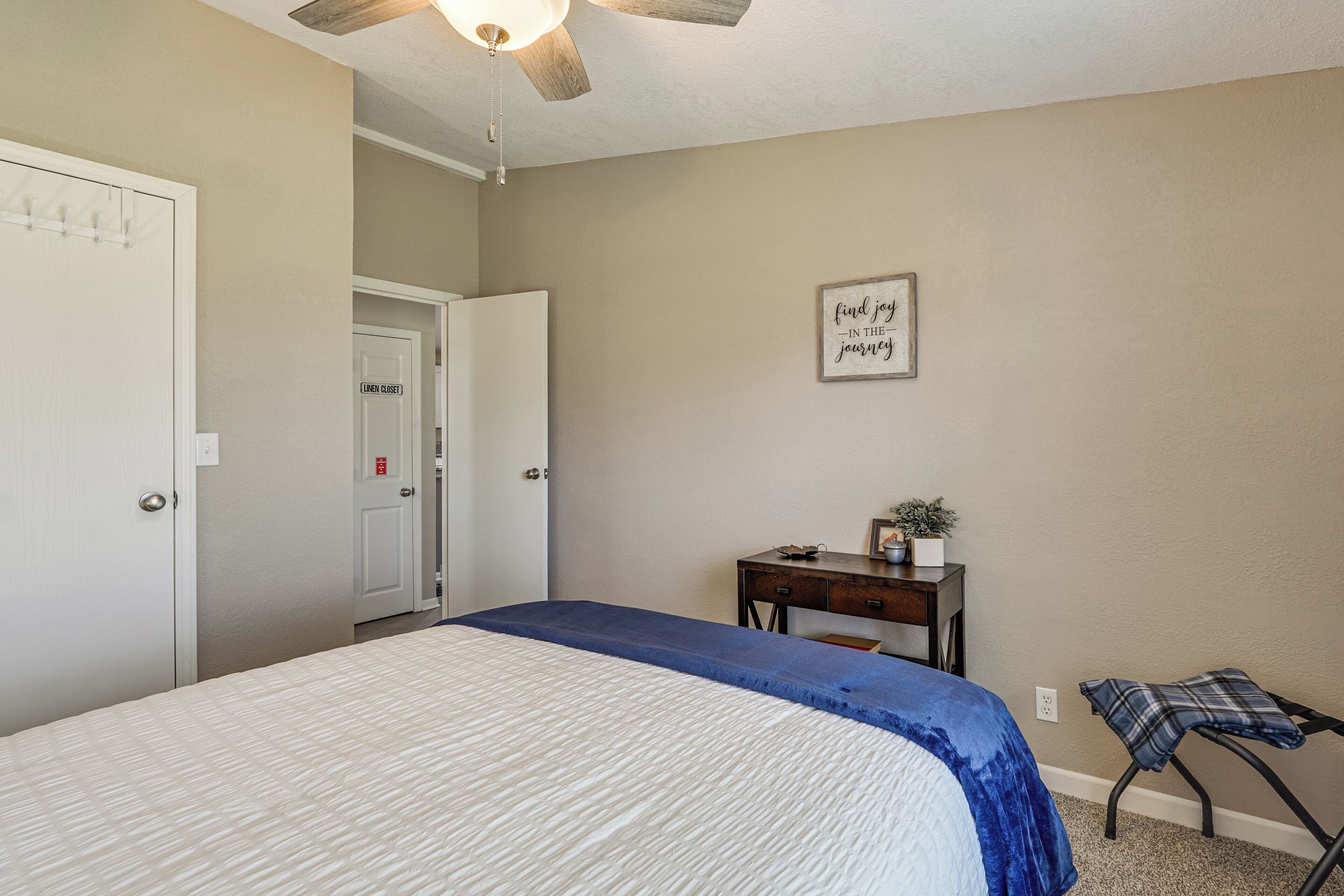 Une chambre à coucher comprenant un lit, un bureau, une chaise, un ventilateur de plafond et une porte donnant sur une autre pièce.