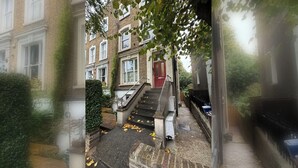 Un edificio residencial con puerta roja, una escalera que lleva a la entrada y fachada de ladrillo.