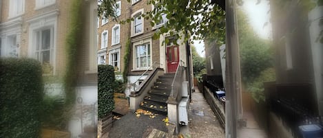 A residential building with a red door, a staircase leading to the entrance, and a brick facade.