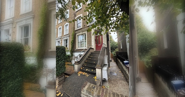 A residential building with a red door, a staircase leading to the entrance, and a brick facade.