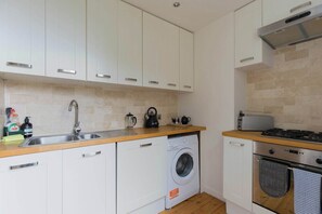 A compact kitchen with white cabinets, a washing machine, a stove, and a sink.