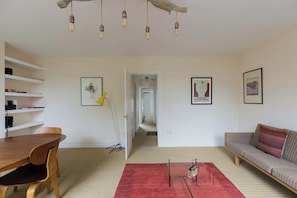 A living room with a wooden dining table, a sofa, a red rug, and a hallway leading to another room.