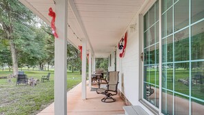 A covered porch with outdoor seating, large windows, and a view of a park.