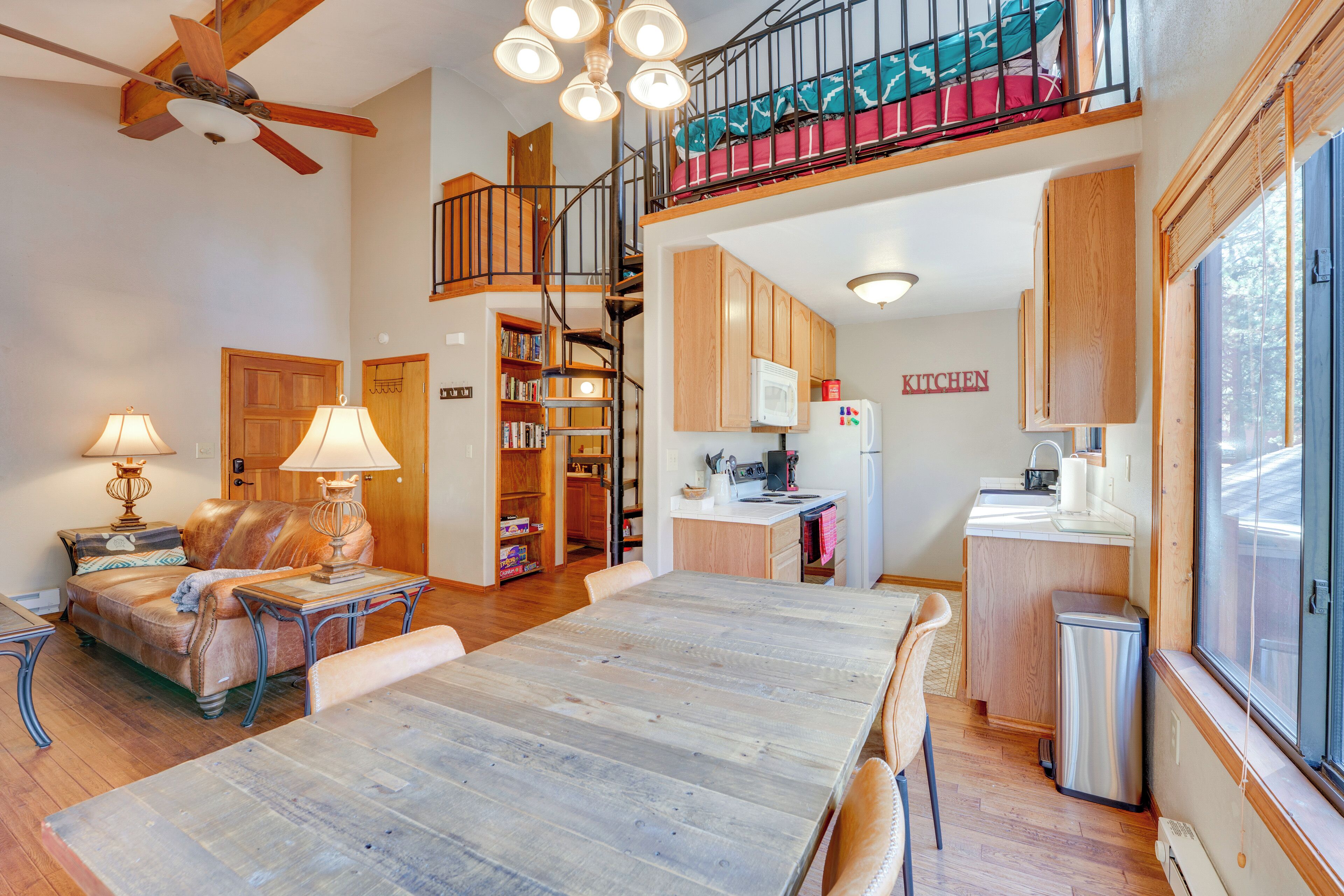 A spacious living area with a wooden dining table, a sofa, and a staircase leading to an upper level.
