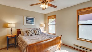 A bedroom with a wooden bed, two bedside lamps, a ceiling fan, a window with blinds, and a framed picture on the wall. - 3 Blocks to Angel Fire Resort: Kid-friendly Condo (Angel Fire)