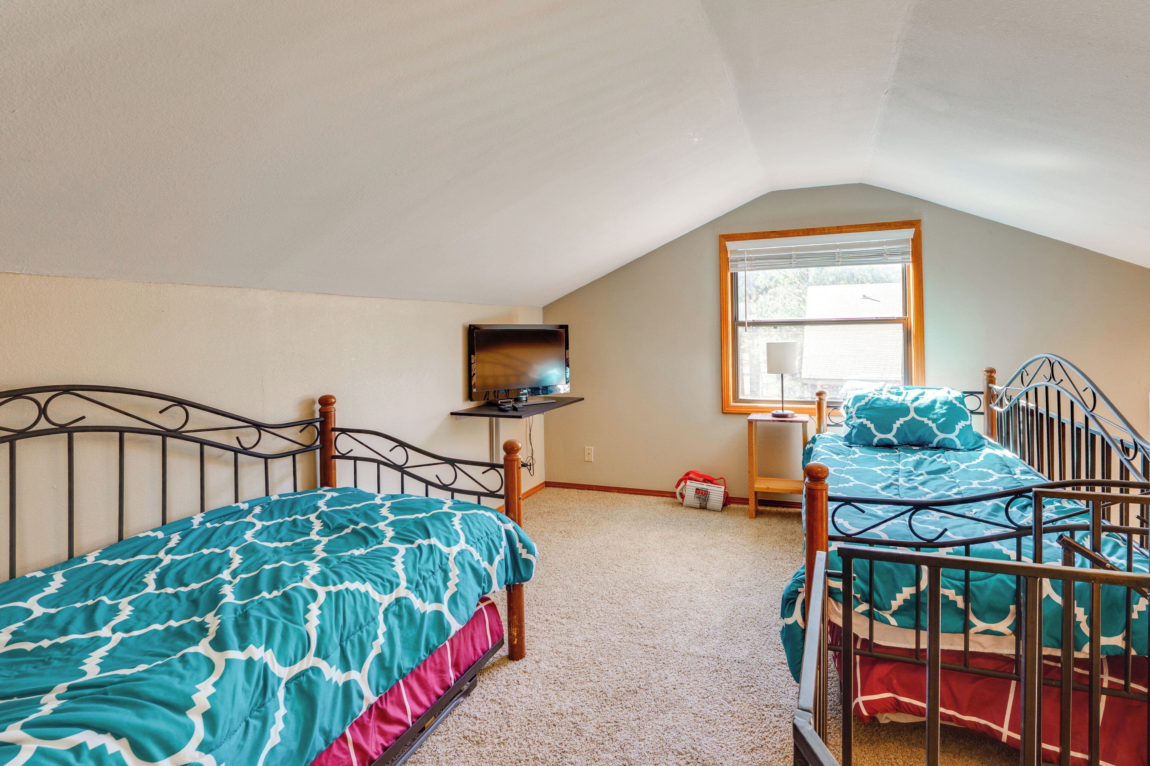 A bedroom with two single beds, a TV, and a window.