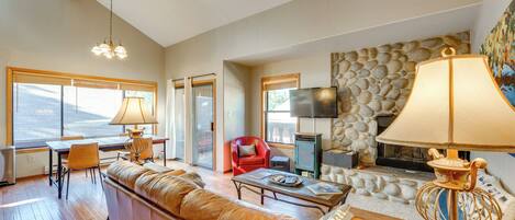 A spacious living room with a leather sofa, a coffee table, and a fireplace. There is a stone wall and a television mounted on the wall.