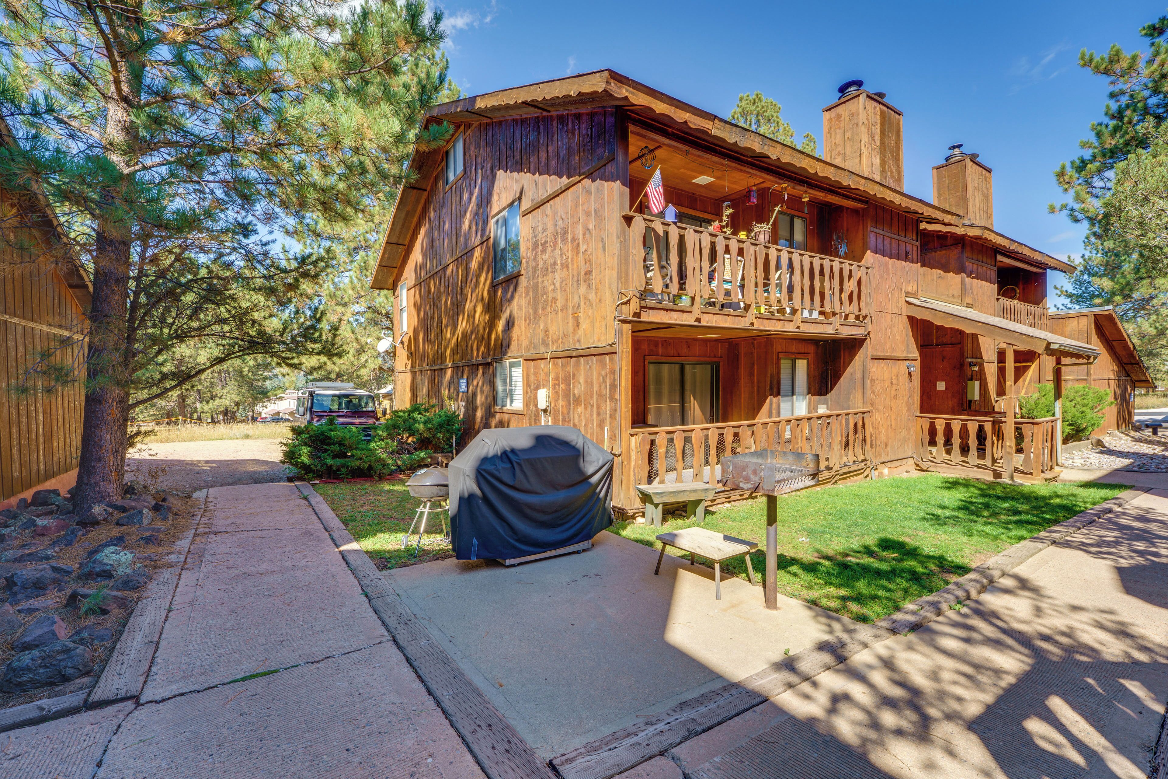 A wooden cabin with a balcony, a covered grill, and a paved driveway.