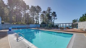 Ein klares, blaues Schwimmbecken mit einer Liegefläche, umgeben von Bäumen und mit Blick auf ein Gewässer.