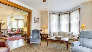 A spacious living room with a patterned carpet, a large armchair, a sofa, and a coffee table. There is a dining area in the background with a table and chairs. - Groups Welcome! Historic Queen Anne Gem in Garrett (Garrett)