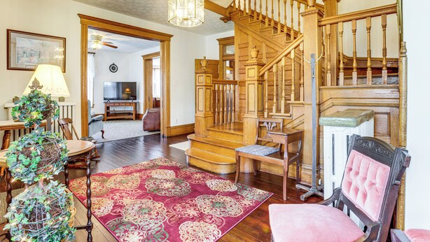 A spacious living room with a wooden staircase, a chandelier, and a red patterned rug. - Groups Welcome! Historic Queen Anne Gem in Garrett (Garrett)
