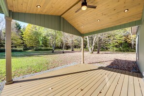 Eine überdachte Holzterrasse mit Deckenventilator, umgeben von Bäumen und einer Rasenfläche.
