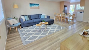 Ein modernes Wohnzimmer mit einem blauen Sofa, einem Couchtisch und einem Essbereich mit Holzsesseln und einem Tisch.