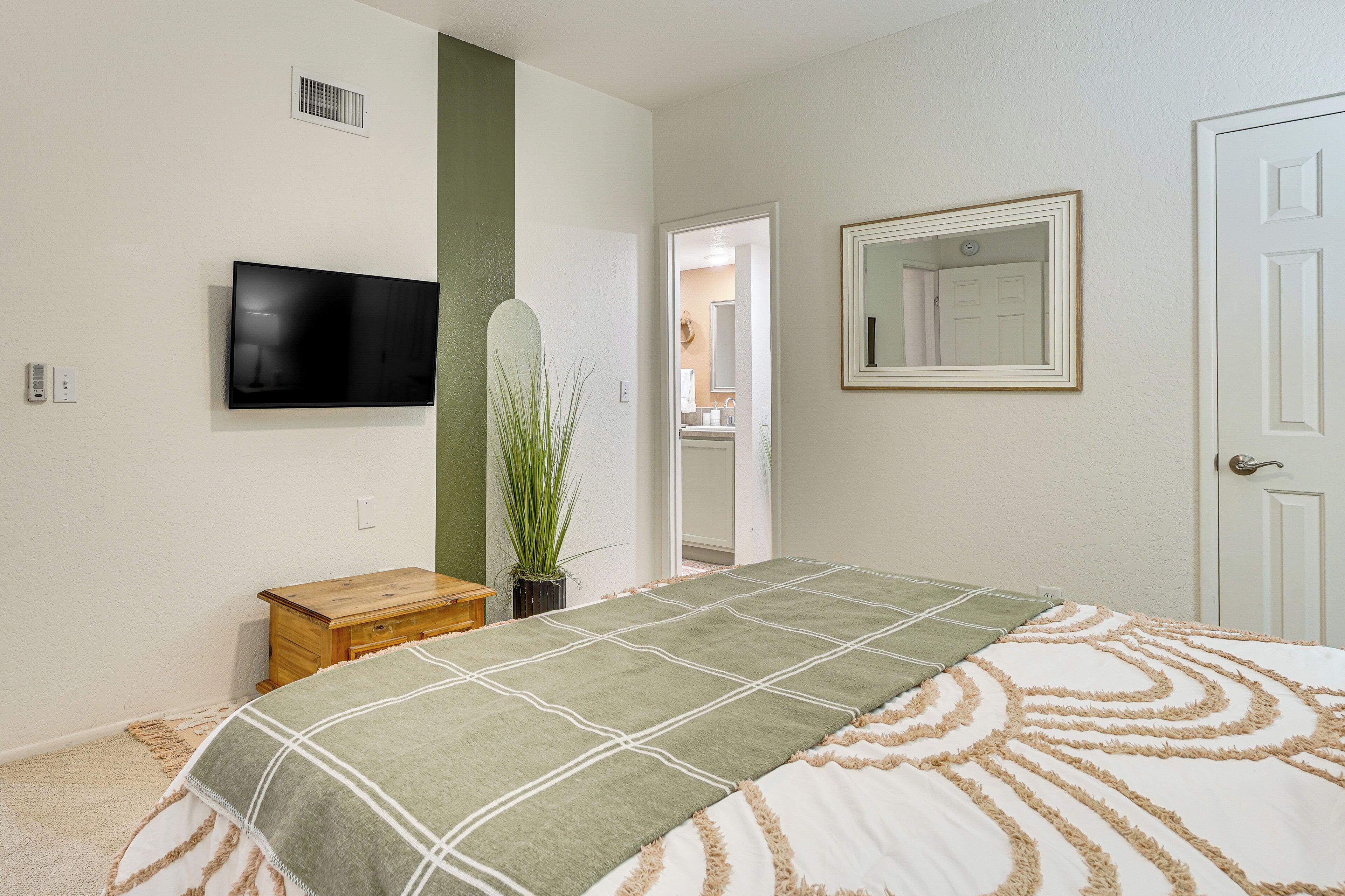 A bedroom with a bed, a television mounted on the wall, a mirror, and a door leading to a bathroom.