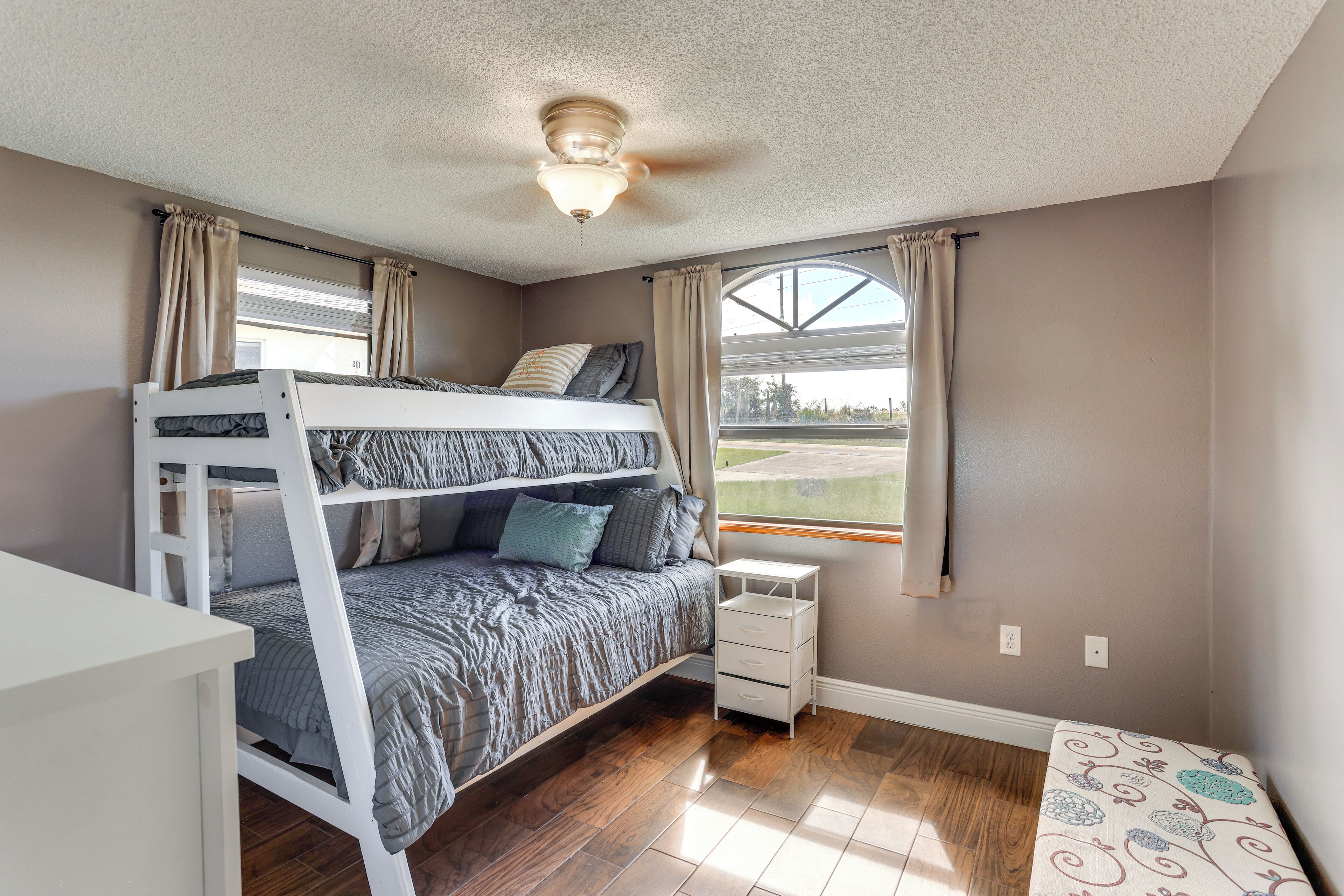 A bedroom with a bunk bed, a small bedside table, a ceiling fan, and a window with curtains.