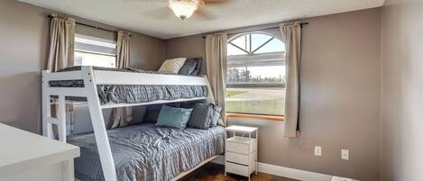 A bedroom with a bunk bed, a small bedside table, a ceiling fan, and a window with curtains.