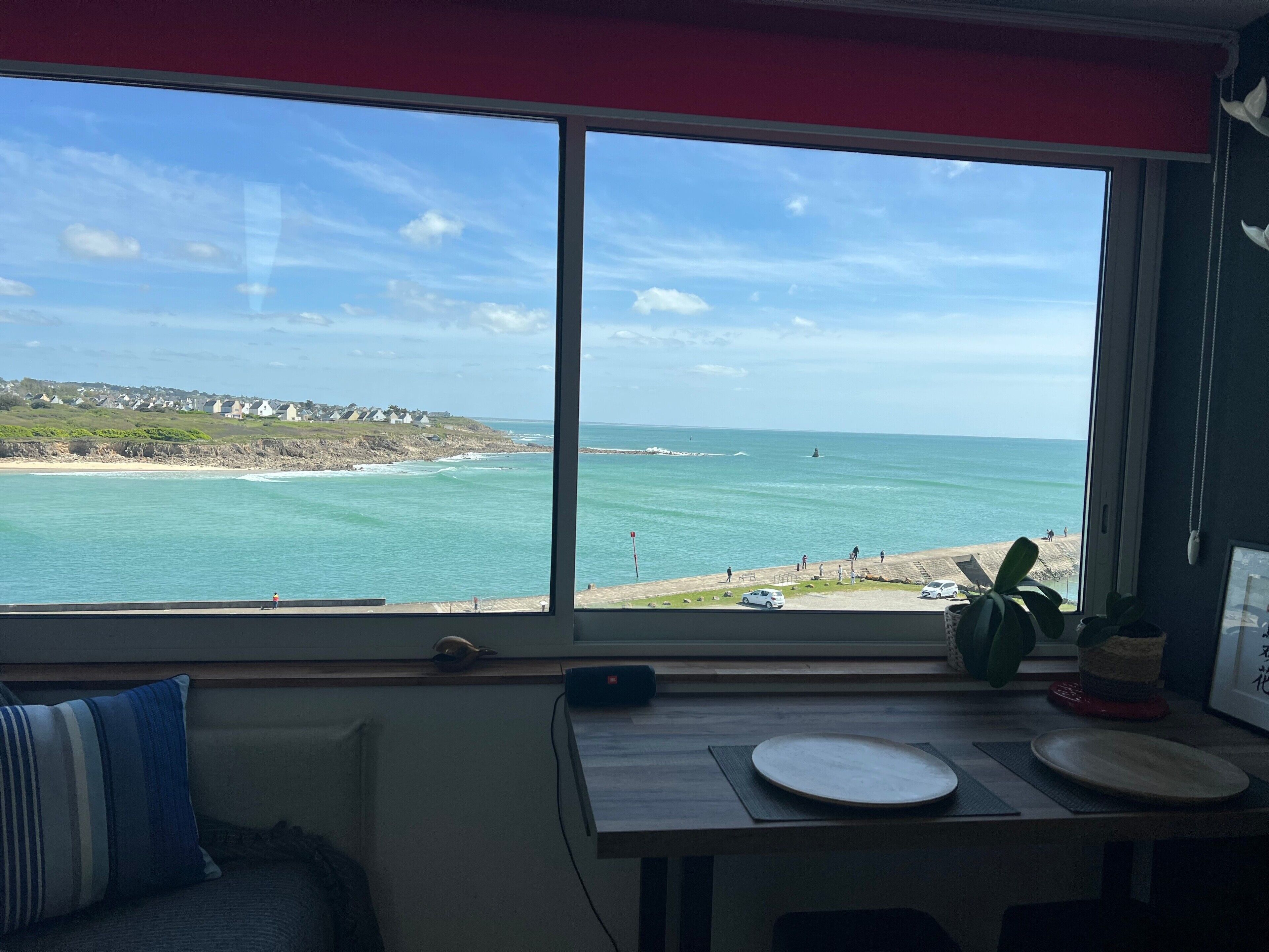 Una stanza con una grande finestra vista spiaggia, un tavolo in legno con piatti e un divano con cuscini a righe.