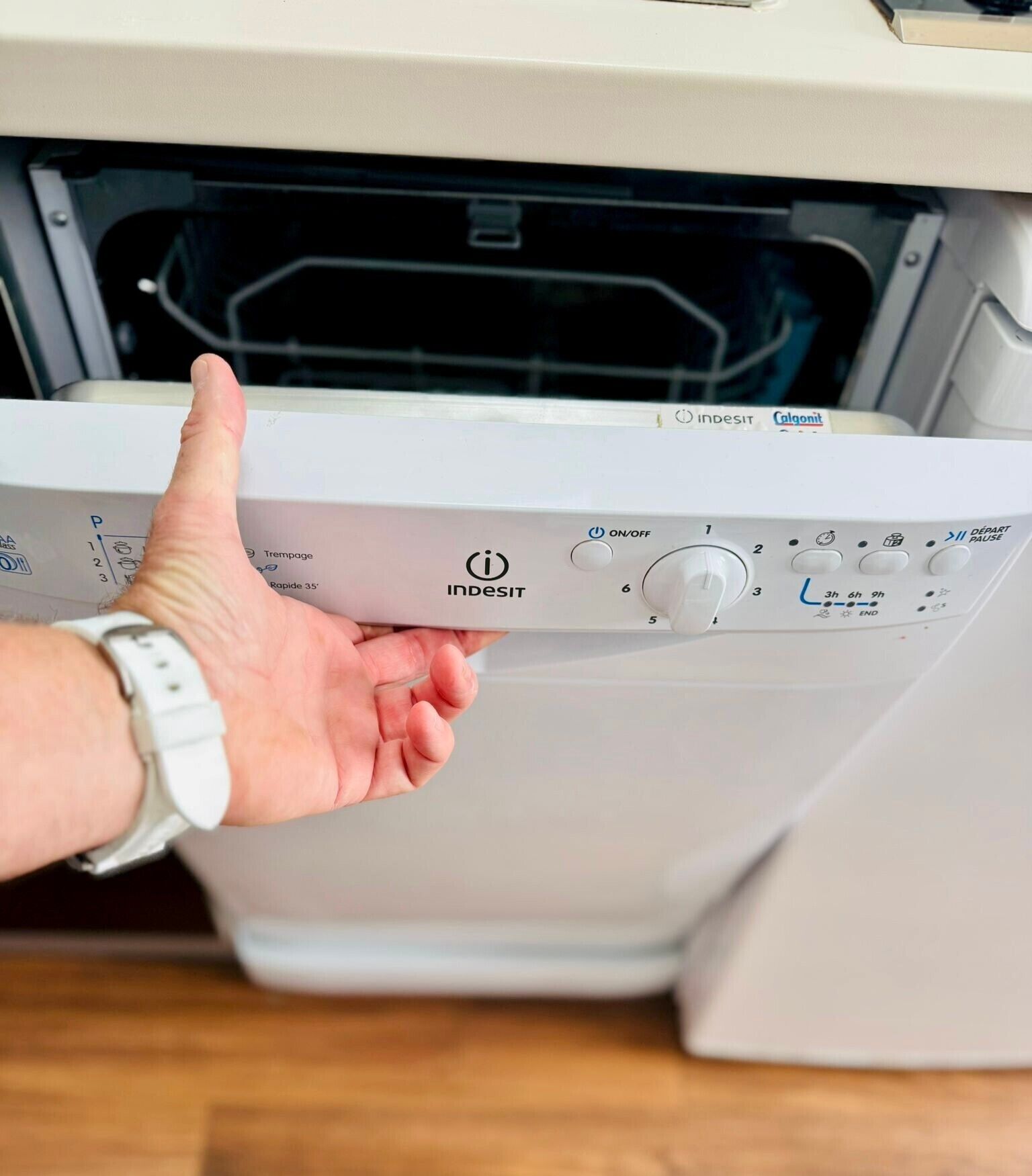 A person operating a white Indesit washing machine with a control panel featuring a power switch, timer, and various settings.