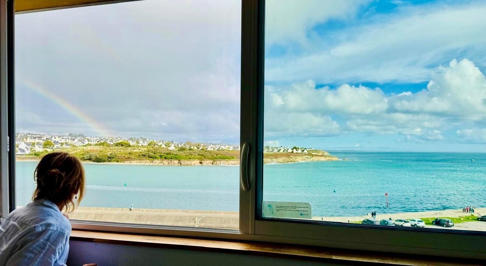 Vista de una zona costera con playa, un arcoíris y una línea de costa distante con edificios.