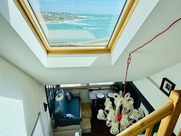 A room with a skylight, a sofa, a dining table, and a hanging light fixture.