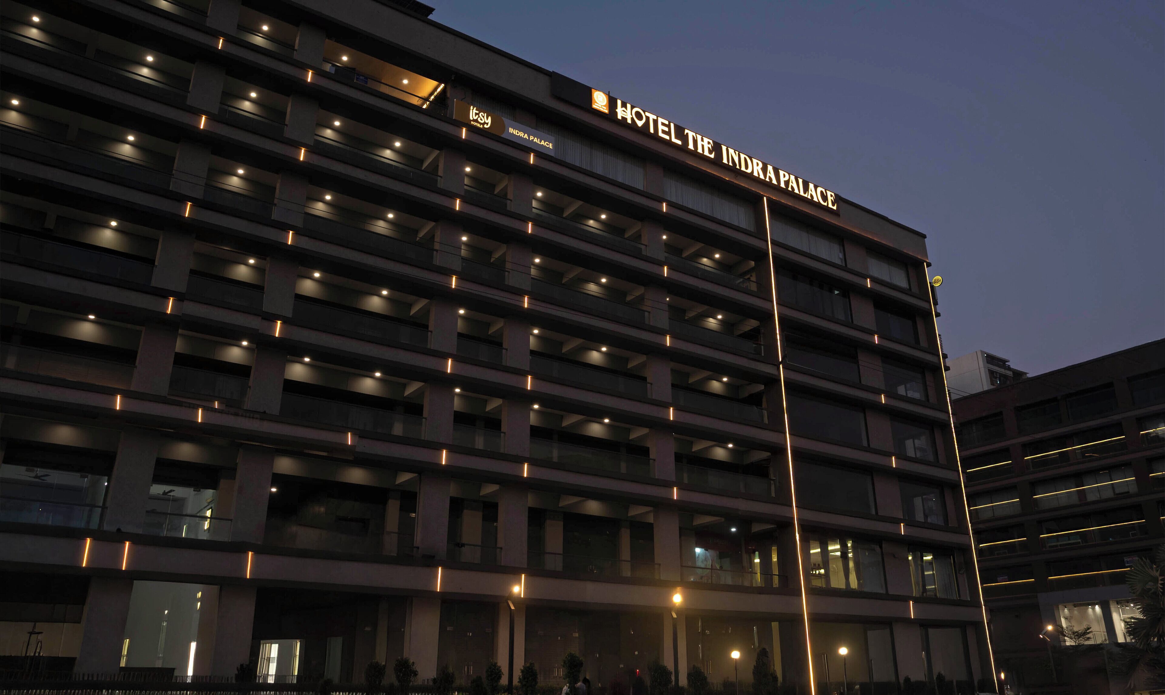 A multi-story hotel building with illuminated signage for "Hotel The Indra Palace."
