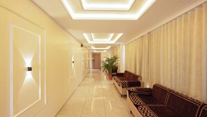 Un couloir d’hôtel avec un long plancher en marbre poli, une rangée de canapés sur le côté droit et une porte au bout.
