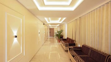 A hotel hallway with a long, polished marble floor, a row of sofas on the right, and a door at the end.