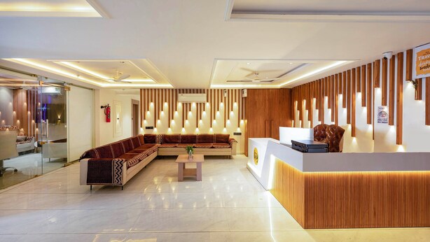 Un hall d’hôtel moderne comprenant un comptoir d’accueil, un espace salon avec des canapés et une cloison en verre séparant le hall des toilettes.