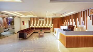 A modern hotel lobby with a reception desk, a seating area with sofas, and a glass partition separating the lobby from the bathroom.