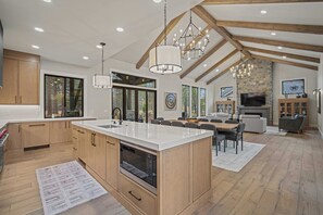 A spacious kitchen with wooden cabinets, a large island, and a dining area with a table and chairs. There is a fireplace and a television in the living area.