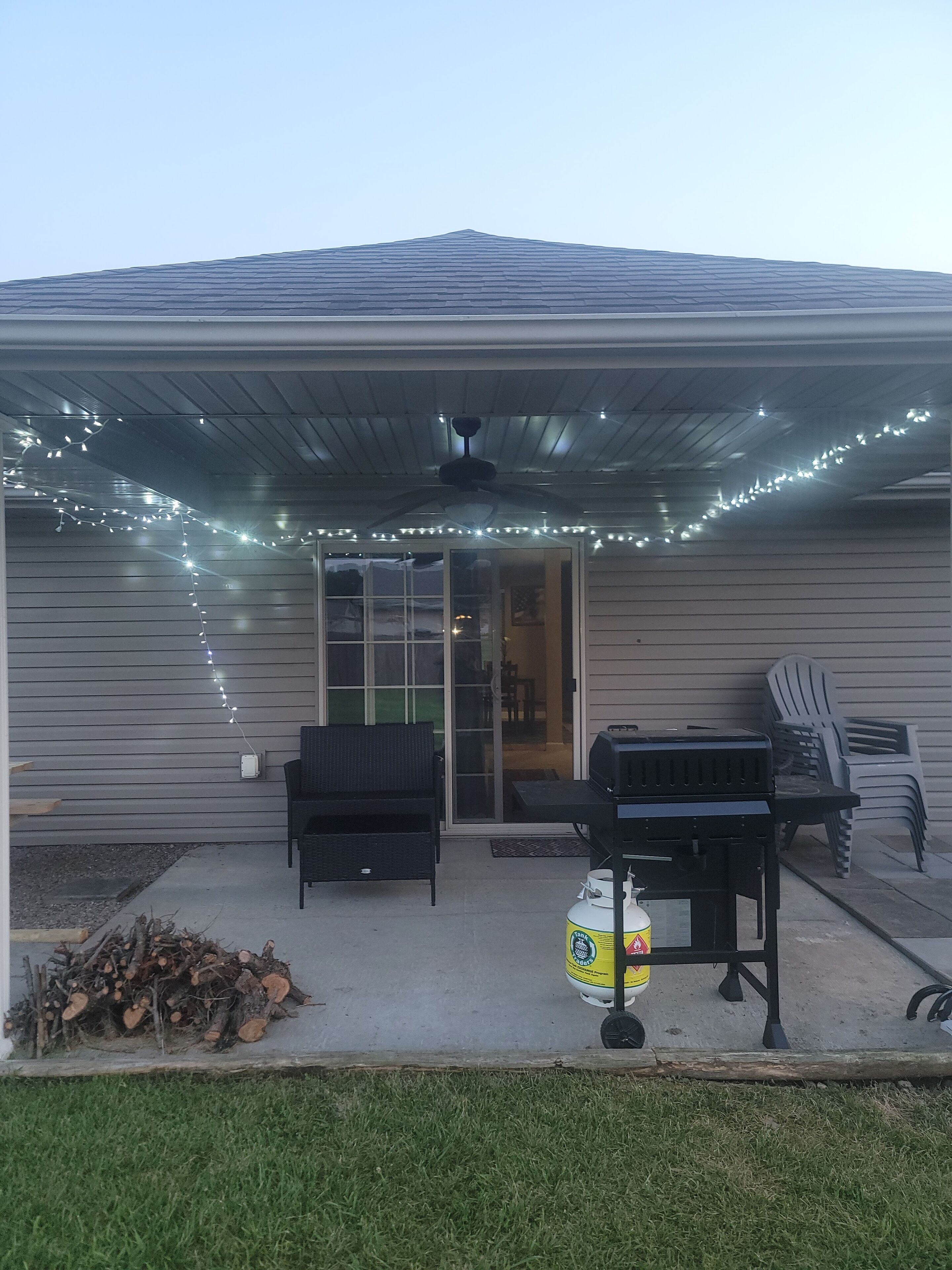 A covered patio area with a ceiling fan, string lights, and a grill.
