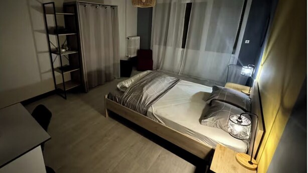 A modern bedroom with a bed, bedside table, lamp, and a wardrobe. - Apartment T1 Paisible (Limoges)