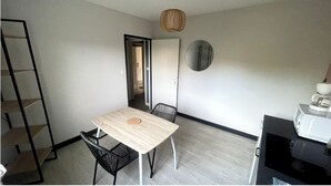 A small, modern kitchen with a table and chairs, a microwave, and a hanging light fixture. - Apartment T1 Paisible (Limoges)