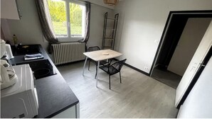 A compact kitchen with a table and chairs, a radiator, and a window with curtains. - Apartment T1 Paisible (Limoges)