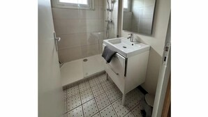 A bathroom with a shower, a sink, a mirror, and a window. - Apartment T1 Paisible (Limoges)