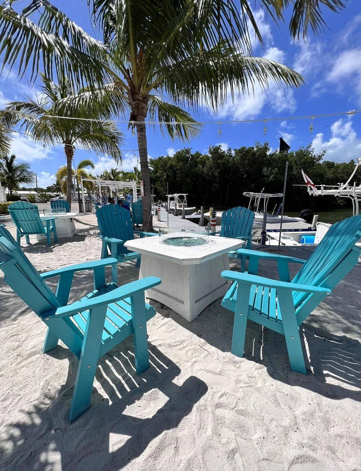 Un espace de détente aménagé au bord de la plage, avec des fauteuils Adirondack turquoise, une table en béton et une piscine.
