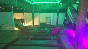 A thatched-roof outdoor seating area with lounge chairs and a table, surrounded by a wooden deck and a stone pathway. - Cozy campground in tranquil Key Largo (Key Largo)