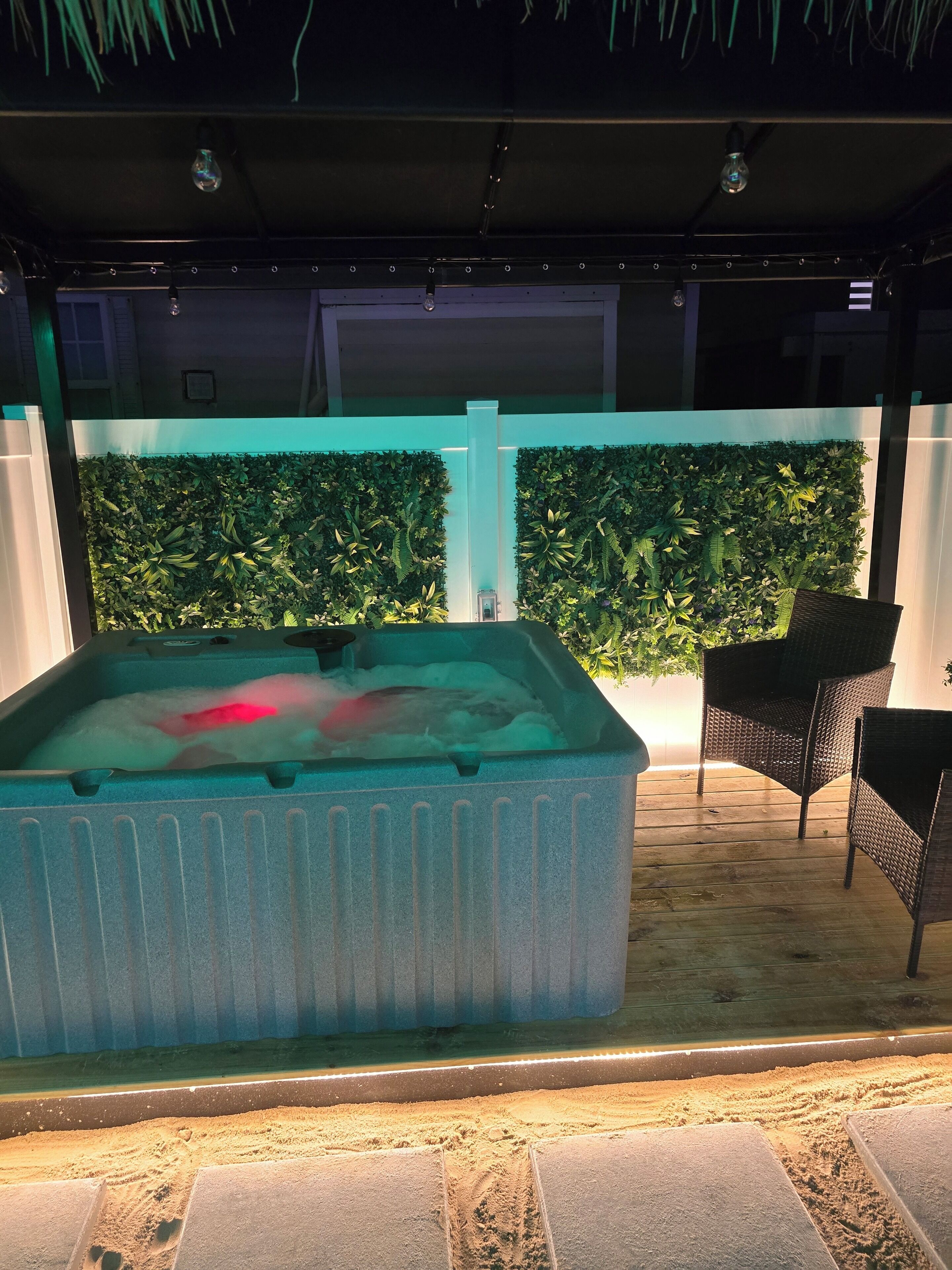 Un bain à remous à l’extérieur texturé, entouré d’une terrasse en bois et d’un mur recouvert d’un jardin vertical.
