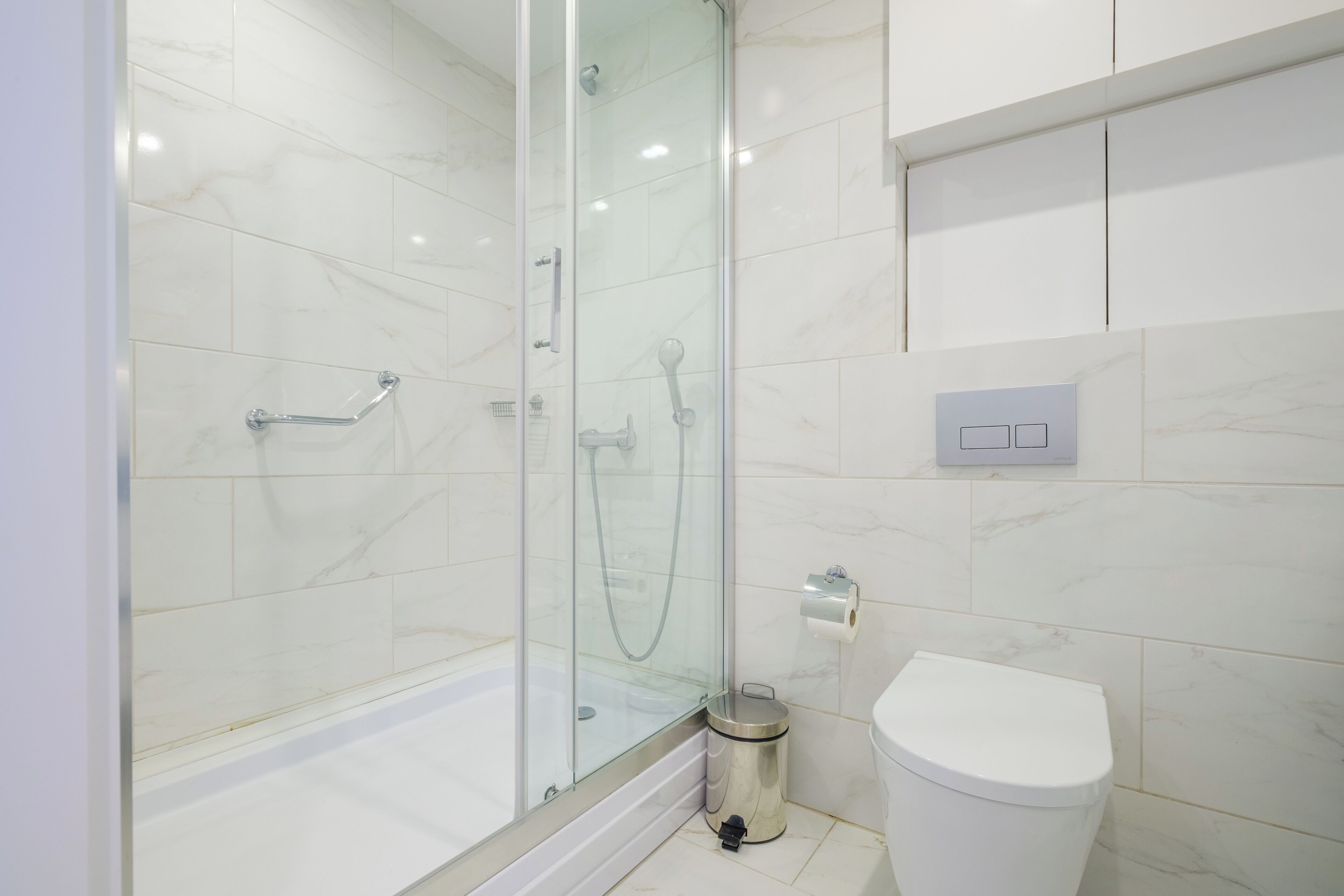 A modern bathroom with a glass-enclosed shower, a white toilet, and a marble-tiled wall.