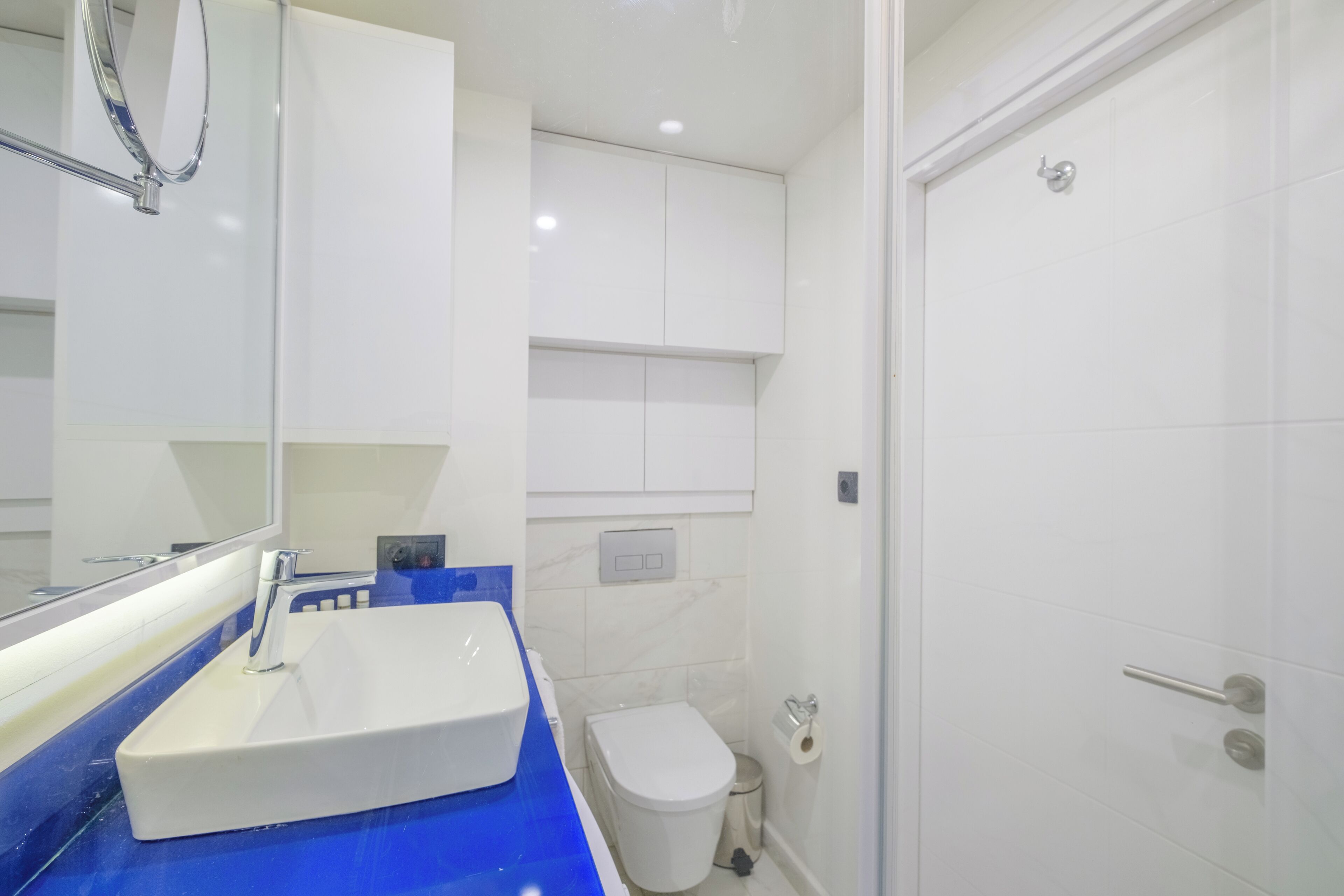 A modern bathroom with a white sink, blue countertop, and a white toilet.