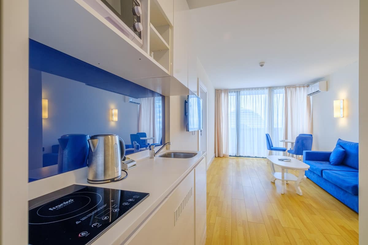 Een moderne keuken met een inbouwfornuis, een spoelbak en een zithoek met een blauwe bank en een kleine tafel.